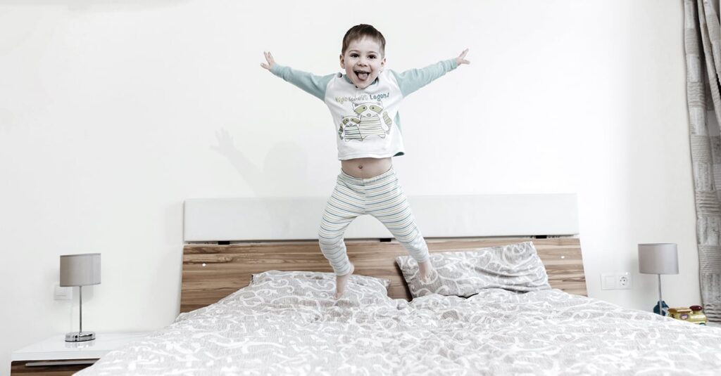 Kind springend op bed — beddengoed van Kessels